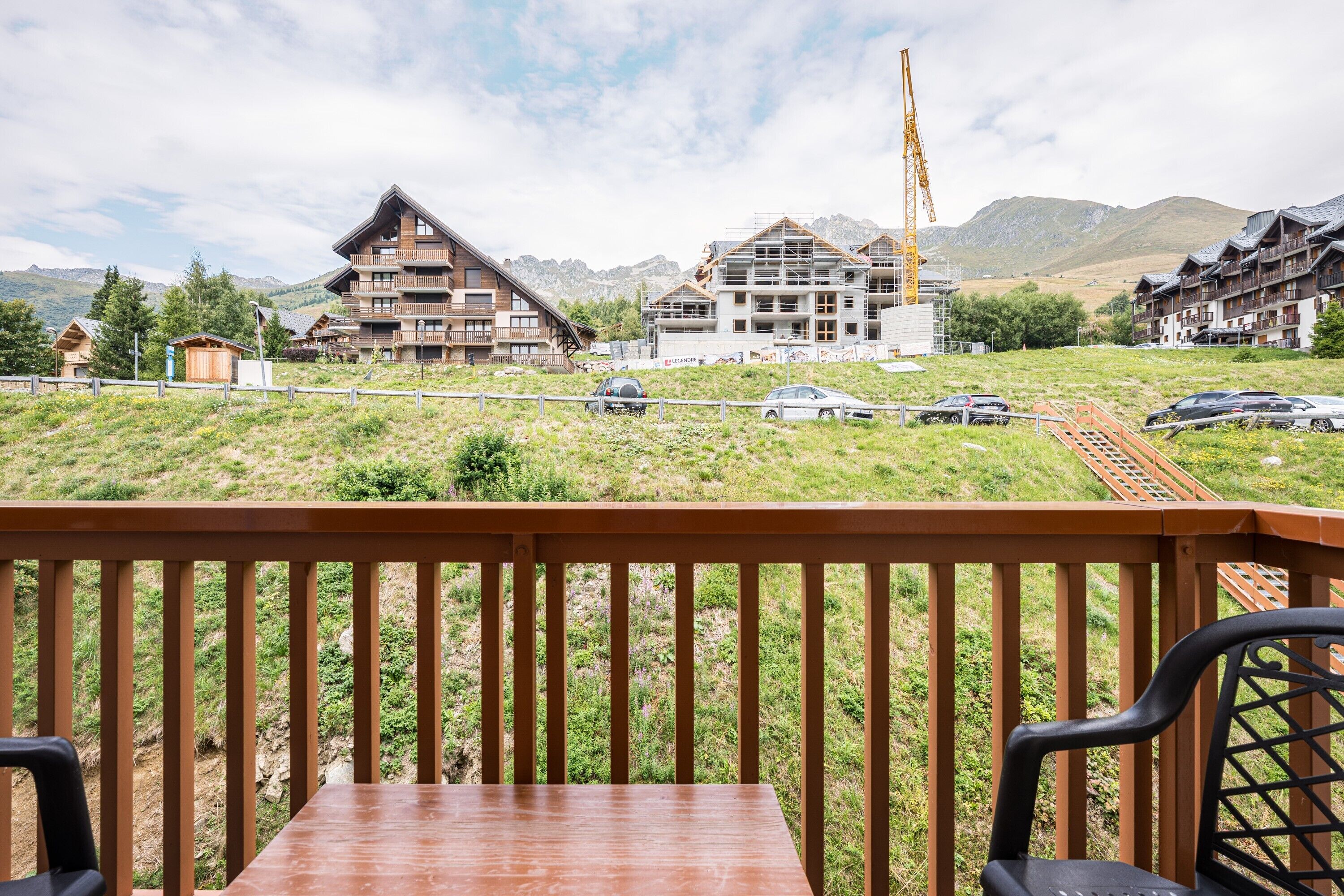 Een houten terras met een tafel en stoelen, met uitzicht op een bergachtig gebied met gebouwen in aanbouw en een treinspoor.