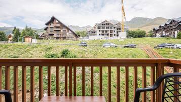 A wooden deck with a table and chairs, overlooking a mountainous area with buildings under construction and a train track.