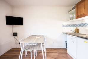 Une cuisine avec une table en bois, des chaises blanches, un lave-vaisselle et un téléviseur fixé au mur.