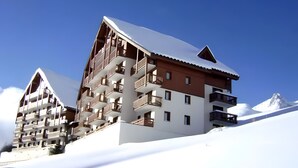 A multi-story hotel with balconies, set against a snowy mountain backdrop.