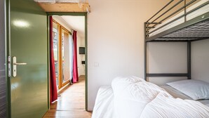 A bunk bed with white bedding, a green door, and a wooden ceiling.