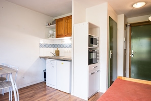 Une cuisine de taille réduite, dotée d’appareils électroménagers blancs, d’un meuble en bois et d’un revêtement mural en carreaux.