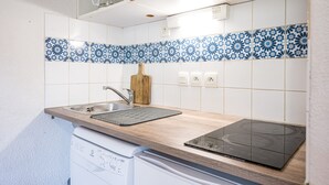 A kitchen with a dishwasher, a sink, a wooden countertop, a black induction cooktop, and blue and white patterned backsplash tiles.