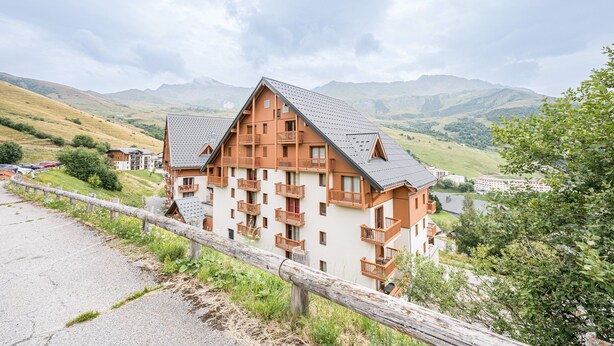 A chalet-style hotel with multiple balconies, a sloped roof, and a view of the surrounding mountains.