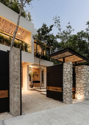 A modern house with a stone wall, a wooden deck, and a covered patio. - Casa Cascada Jungle Villa Beach Club Access (Tulum)