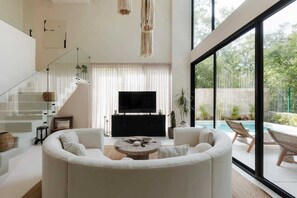 A modern living room with a sofa set, a coffee table, a TV, and a staircase. - Casa Cascada Jungle Villa Beach Club Access (Tulum)