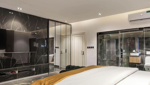 A modern hotel room with a large bed, a glass-enclosed walk-in closet, a separate bathroom, and a mounted television. - Bromford Hotel (Owerri)