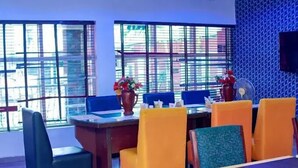 A dining area with a table and chairs, a vase with flowers, and a window with blinds. - Bromford Hotel (Owerri)