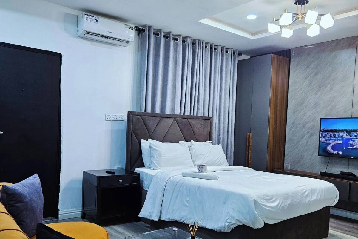 A modern hotel room with a large bed, a flat-screen TV, a glass coffee table, and a sofa.