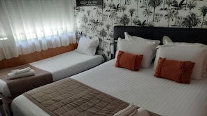 Quarto de hotel com duas camas, roupa de cama branca e castanha, e papel de parede tropical.