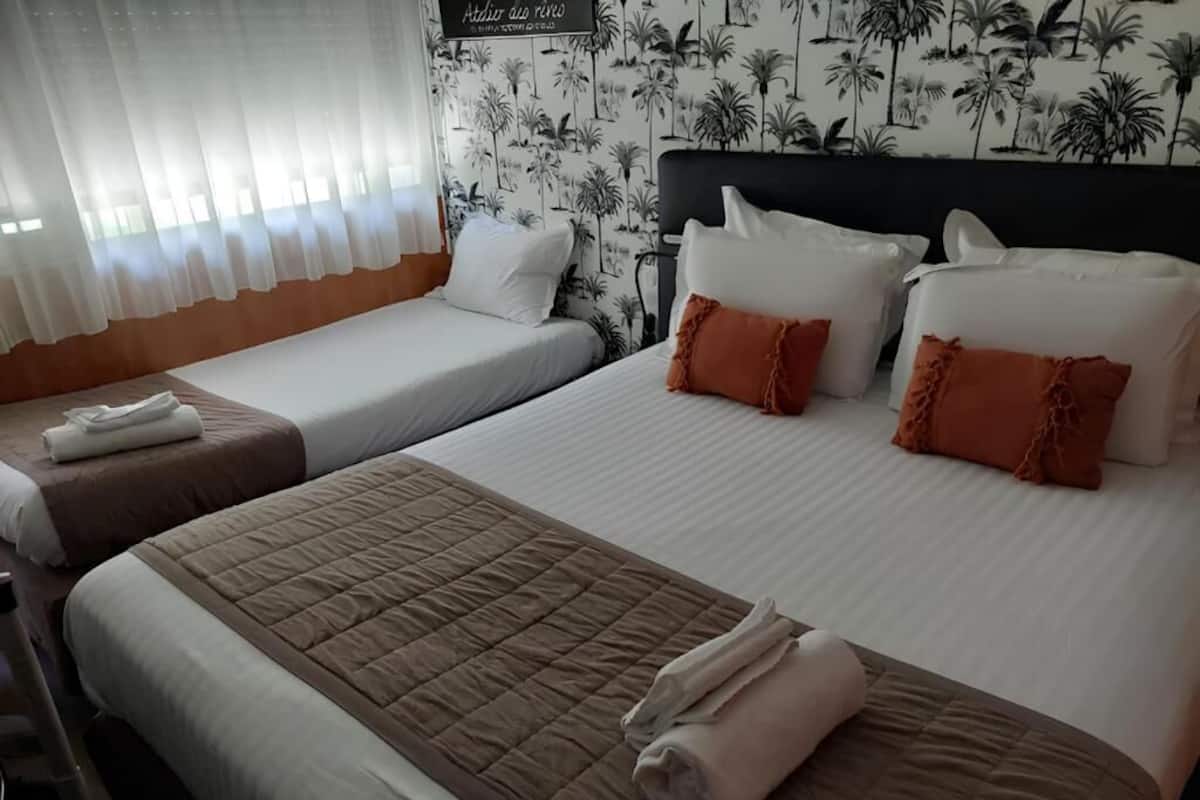 A hotel room with two beds, white and brown bedding, and a tropical wallpaper.