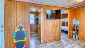 A room with wooden walls, a bunk bed, a television, and surfboards.
