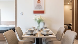A dining area with a table set for four, surrounded by cushioned chairs, a vase with flowers, and a modern air conditioning unit above.