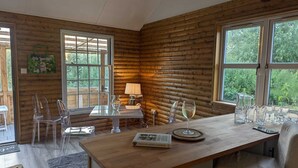 Un interior acogedor de cabaña, con revestimiento de madera, una mesa de comedor con sillas, una lámpara y un libro titulado 'INDOOR GARDEN'.