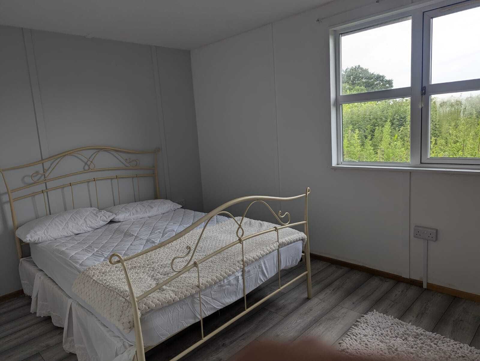 A bedroom with a single bed, a window with a view of greenery, and a wooden floor.