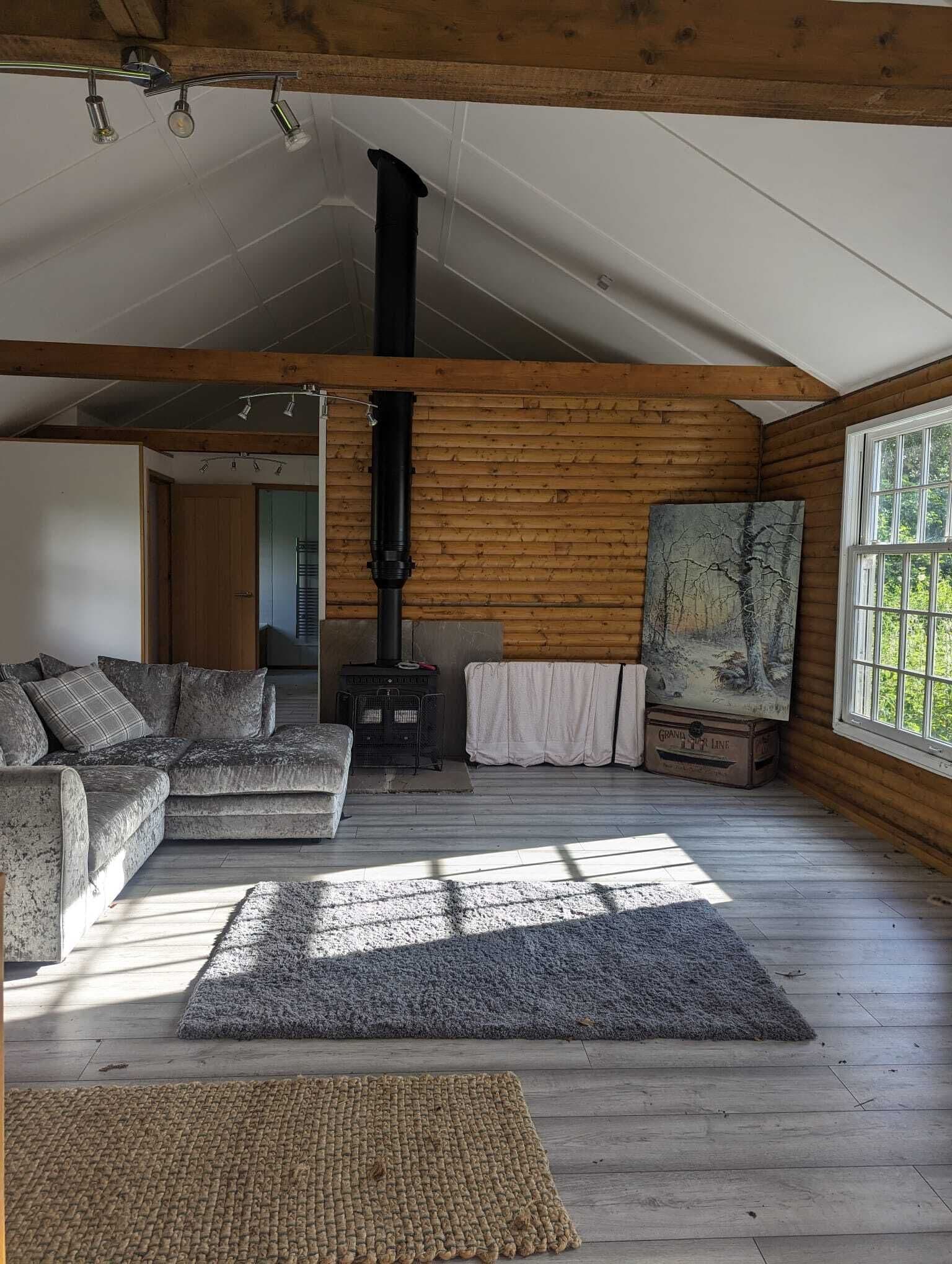 Un interior d'una cabana acollidora, amb decoració de fusta, una llar de foc, un sofà i un quadre a la paret.