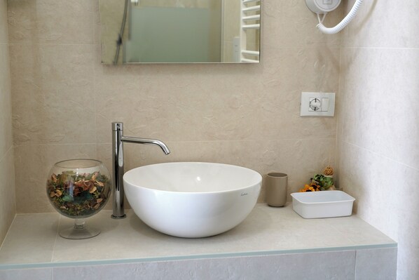 A bathroom with a white sink, a glass bowl, and a small white container.