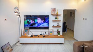 A modern living room with a large flat-screen TV mounted on a white wall, a wooden entertainment unit below, and a hallway leading to another room.