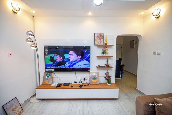 A modern living room with a large flat-screen TV mounted on a white wall, a wooden entertainment unit below, and a hallway leading to another room.