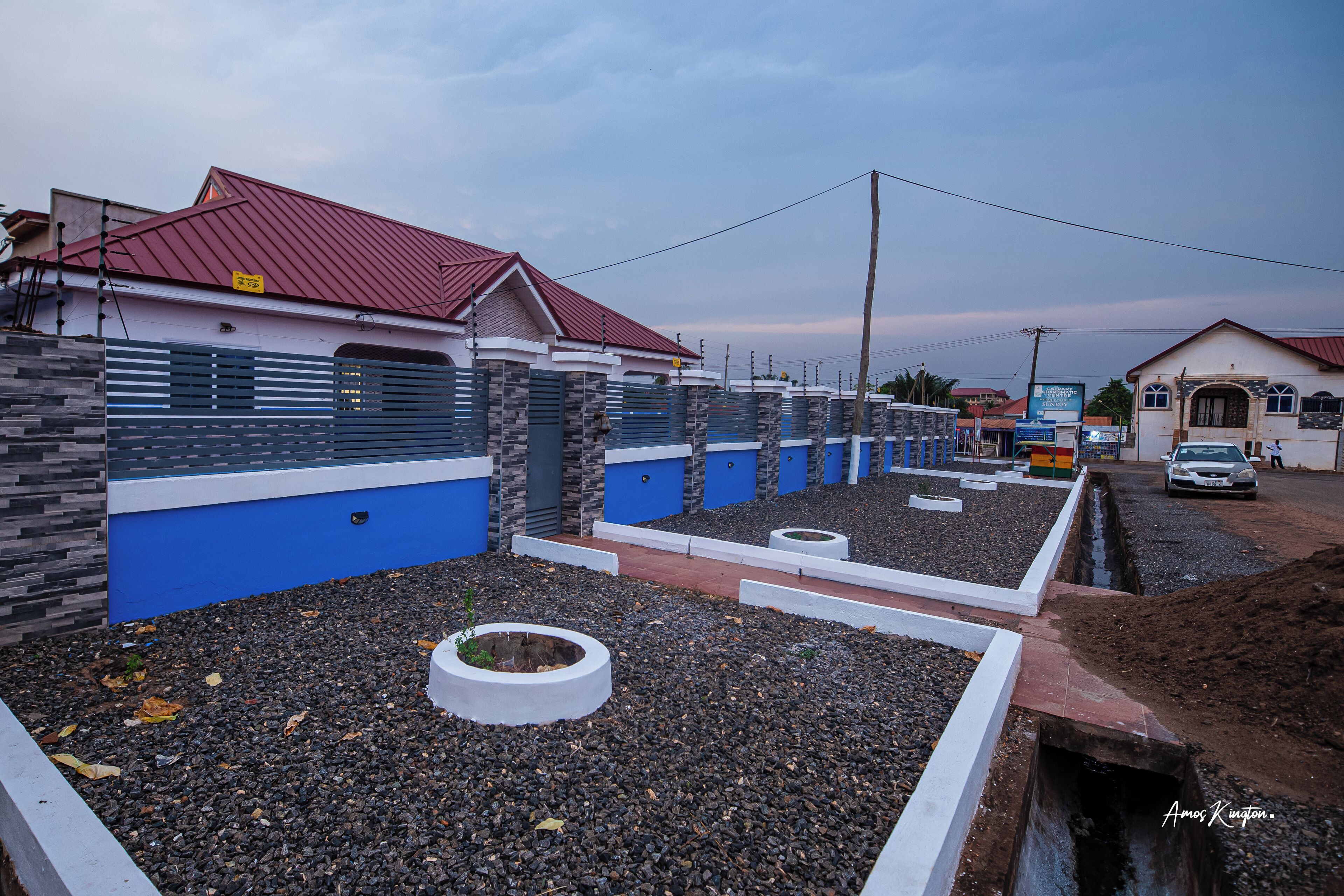 A residential area with modern houses featuring blue and white walls, red roofs, and a well-maintained garden area with gravel and circular planters.
