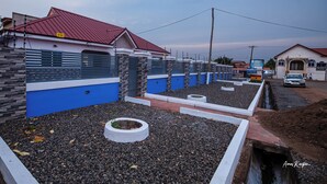 A residential area with modern houses featuring blue and white walls, red roofs, and a well-maintained garden area with gravel and circular planters.