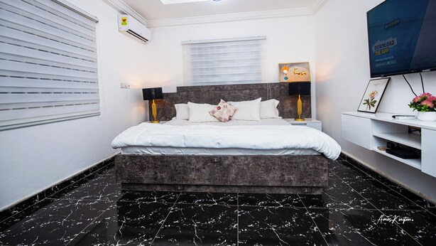 A modern bedroom with a bed, a ceiling light, a TV, and a wall-mounted shelf.