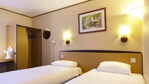Habitación de hotel con dos camas, cabecero de madera, un cuadro en la pared y dos lámparas de pared.
