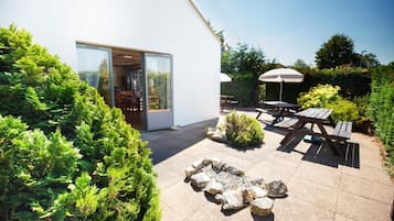 Un patio exterior moderno con un brasero, mesas de picnic y una puerta de vidrio que da a una habitación.