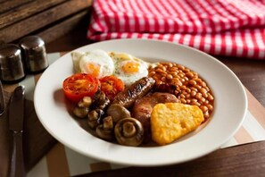 Un plato de desayuno con huevos, salchichas, champiñones, frijoles al horno y una rebanada de tostada.