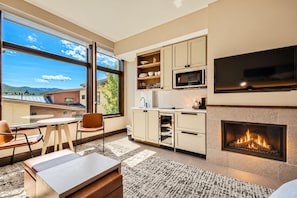 A modern kitchen with a fireplace, large windows, and a dining area. - Charlie Rentz: Remodeled, Fireplace, Ski-In/Out, Ski Valet, Pool + Hot Tubs, Resort Amenities (Avon)