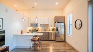 A modern kitchen with a central island, stainless steel appliances, pendant lighting, and a herringbone backsplash.