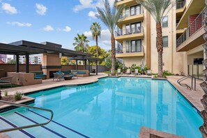A swimming pool with lounge chairs, palm trees, and a multi-story building with balconies. - Boulevard Stays Modern Roosevelt Row Suite 1BR Pool, Gym 1 (Phoenix)