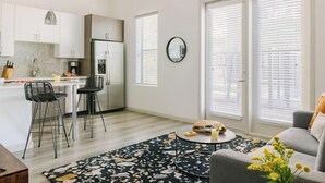A modern apartment with a kitchen, dining area, and living room. It includes a dining table with chairs, a sofa, and a coffee table.