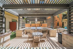 An outdoor patio with a grill, seating, and a pergola structure.