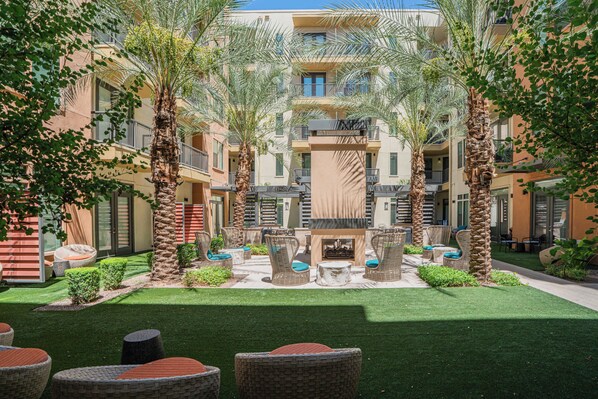 A courtyard with outdoor seating, palm trees, and a central fire pit.