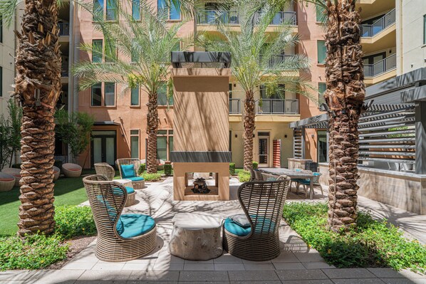 Un patio con mobiliario exterior, palmeras y un edificio con balcones.