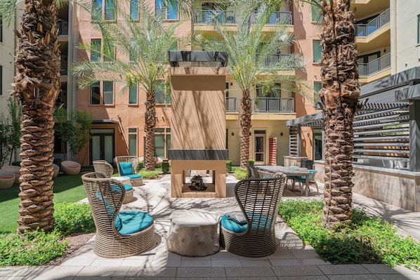 Un patio con mobiliario exterior, palmeras y un edificio con balcones.