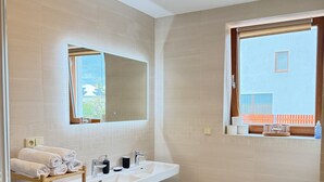 Un bany amb un lavabo, mirall i vàter. Hi ha una barra de tovalloles amb tovalloles i un safata de brossa.