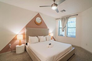 Una camera da letto con un letto, lampade sui comodini, una ventola a soffitto, una finestra con tende e uno specchio fissato alla parete.