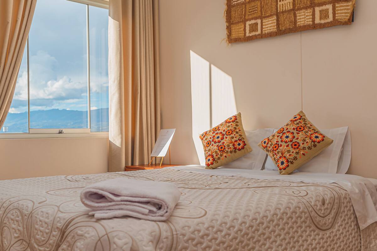 Una habitación de hotel con una cama, una ventana con cortinas, una obra de arte en la pared y una silla.