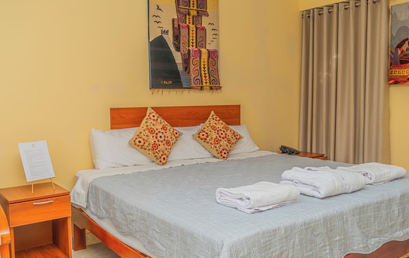 Une chambre d’hôtel avec un lit, des oreillers, une table de chevet, un téléphone et un tableau au mur.