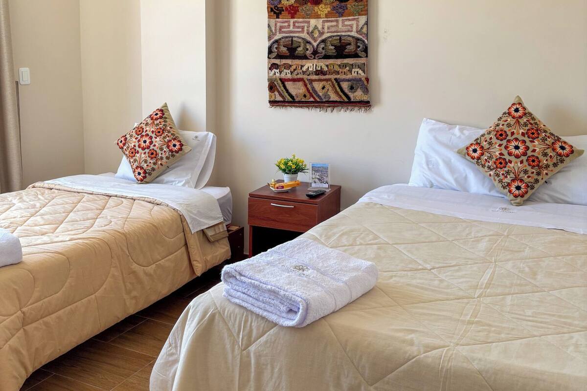Habitación de hotel con dos camas, cada una con colcha beige acolchada y almohada estampada. Un tapiz decorativo cuelga de la pared sobre las camas.