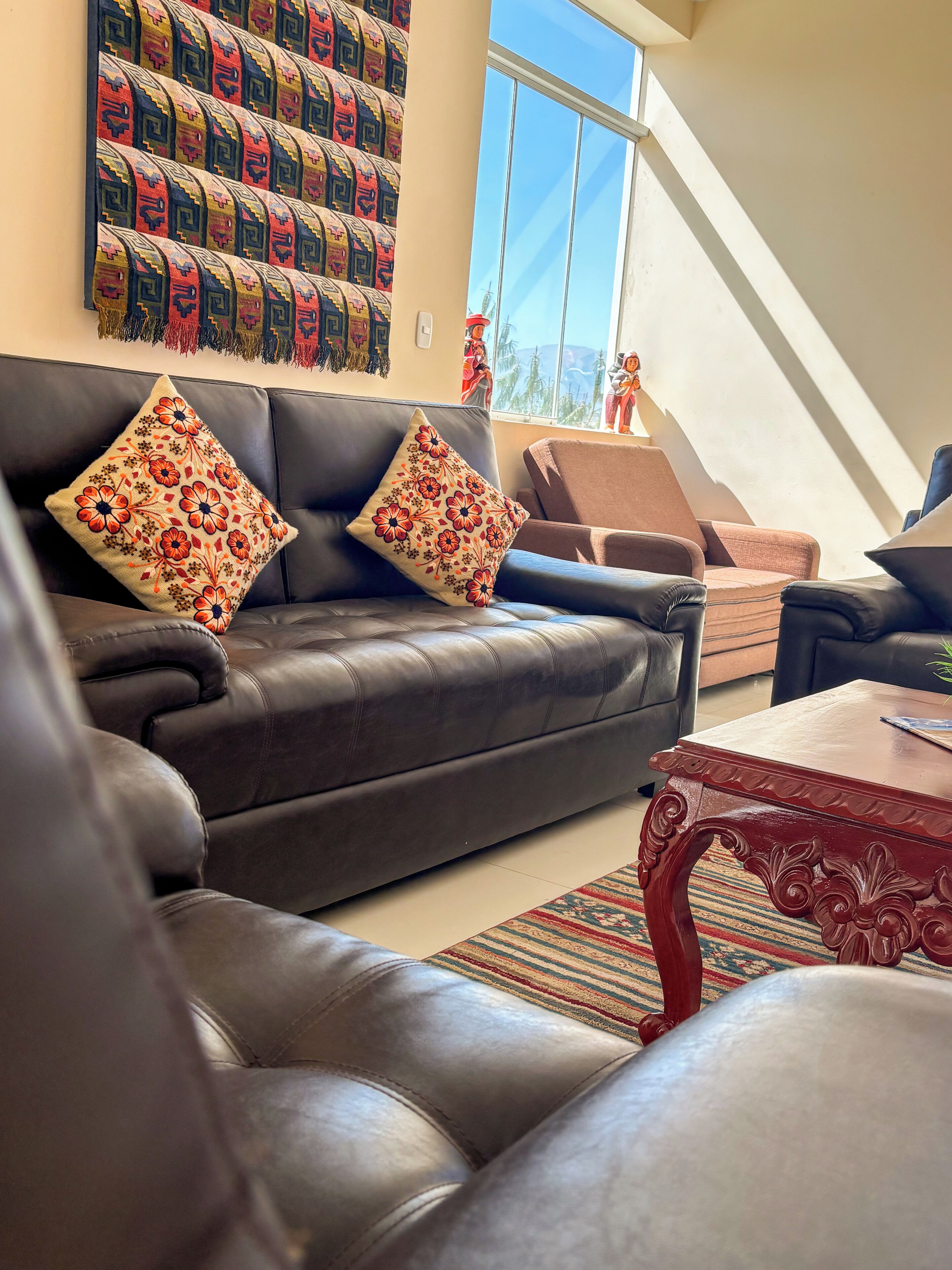 A living room with a dark leather sofa, two decorative pillows, a wooden coffee table, and a patterned rug.