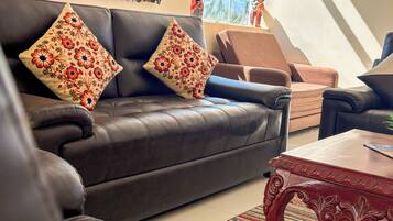 A living room with a dark leather sofa, two decorative pillows, a wooden coffee table, and a patterned rug.