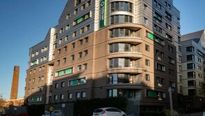 A multi-story hotel with a modern design, featuring a curved facade and a prominent green sign. - McMillan Student Village in London (London)