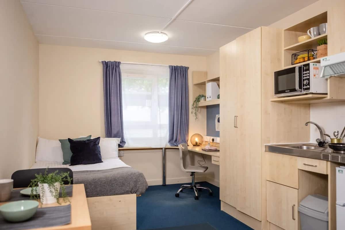 A compact room with a bed, desk, and kitchenette.