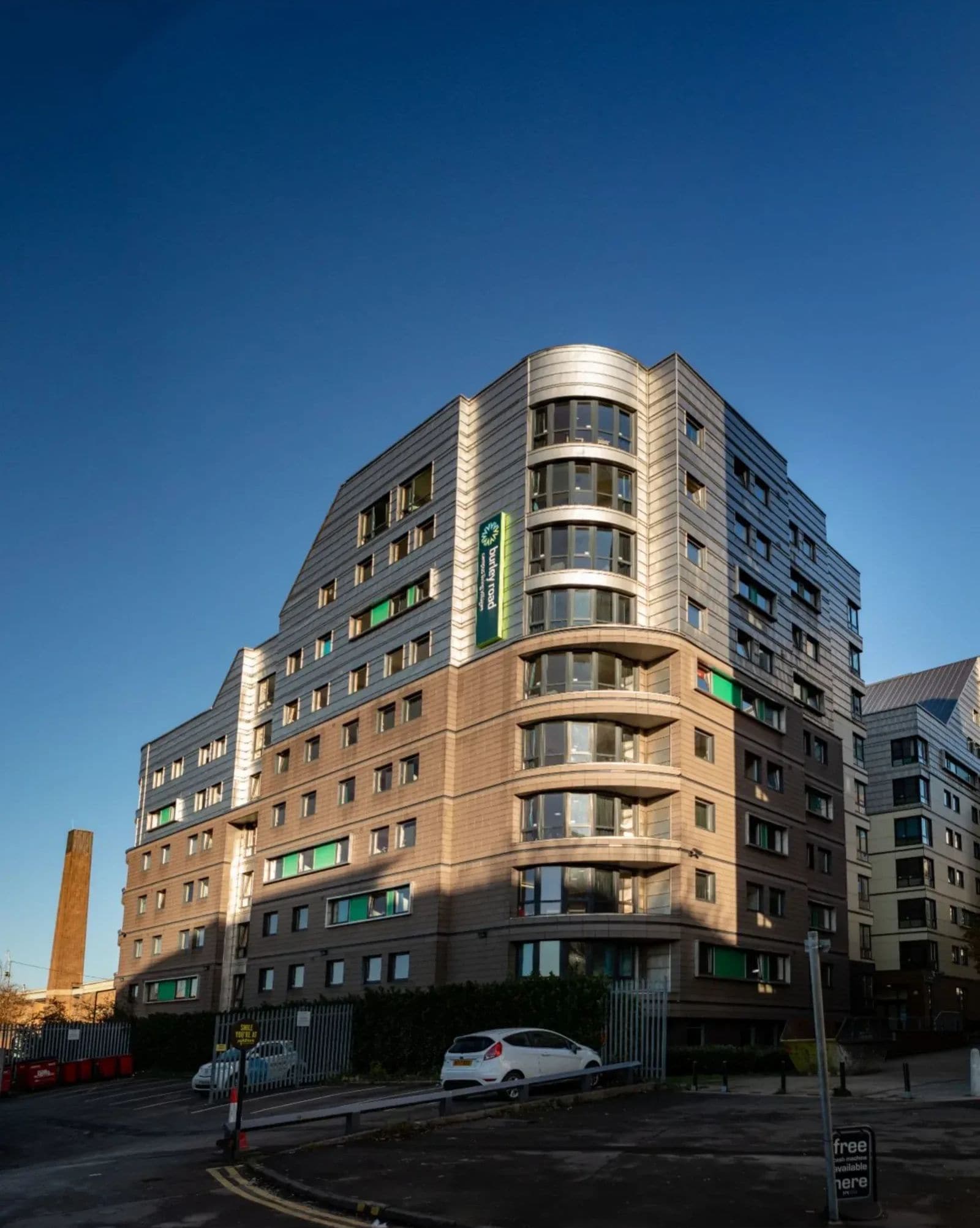 A multi-story hotel with a modern design, featuring a curved facade and a prominent green sign.