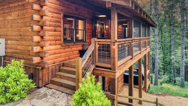 A log cabin with a wooden staircase leading to a deck, surrounded by a forest. - Whimsical Ways - Hot tub-screen porch-pet friendly (Blue Ridge)