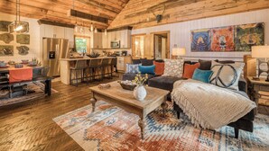 A rustic interior with a wooden ceiling, a kitchen with a stainless steel refrigerator, a dining area with a red tablecloth, and a living room with a sofa and colorful pillows. - Whimsical Ways - Hot tub-screen porch-pet friendly (Blue Ridge)