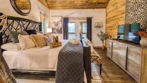 A log cabin-style bedroom with a bed, bedside table, TV, and a view of the outdoors. - Whimsical Ways - Hot tub-screen porch-pet friendly (Blue Ridge)
